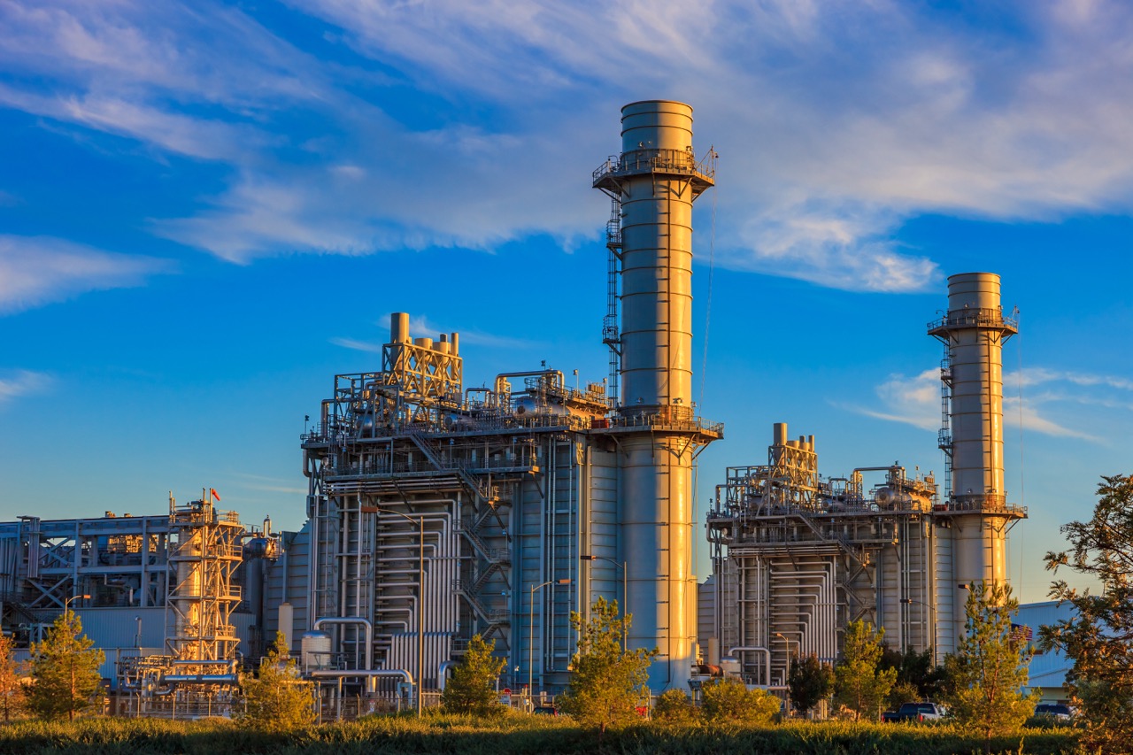 Natural gas fired turbine power plant with it's cooling towers rising into a cloud filled blue sky